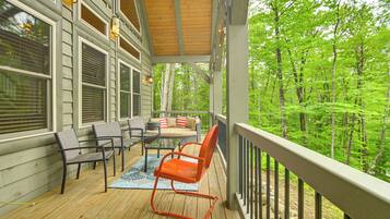 A wooden deck with outdoor furniture, a covered area with a railing, and a view of a forest.