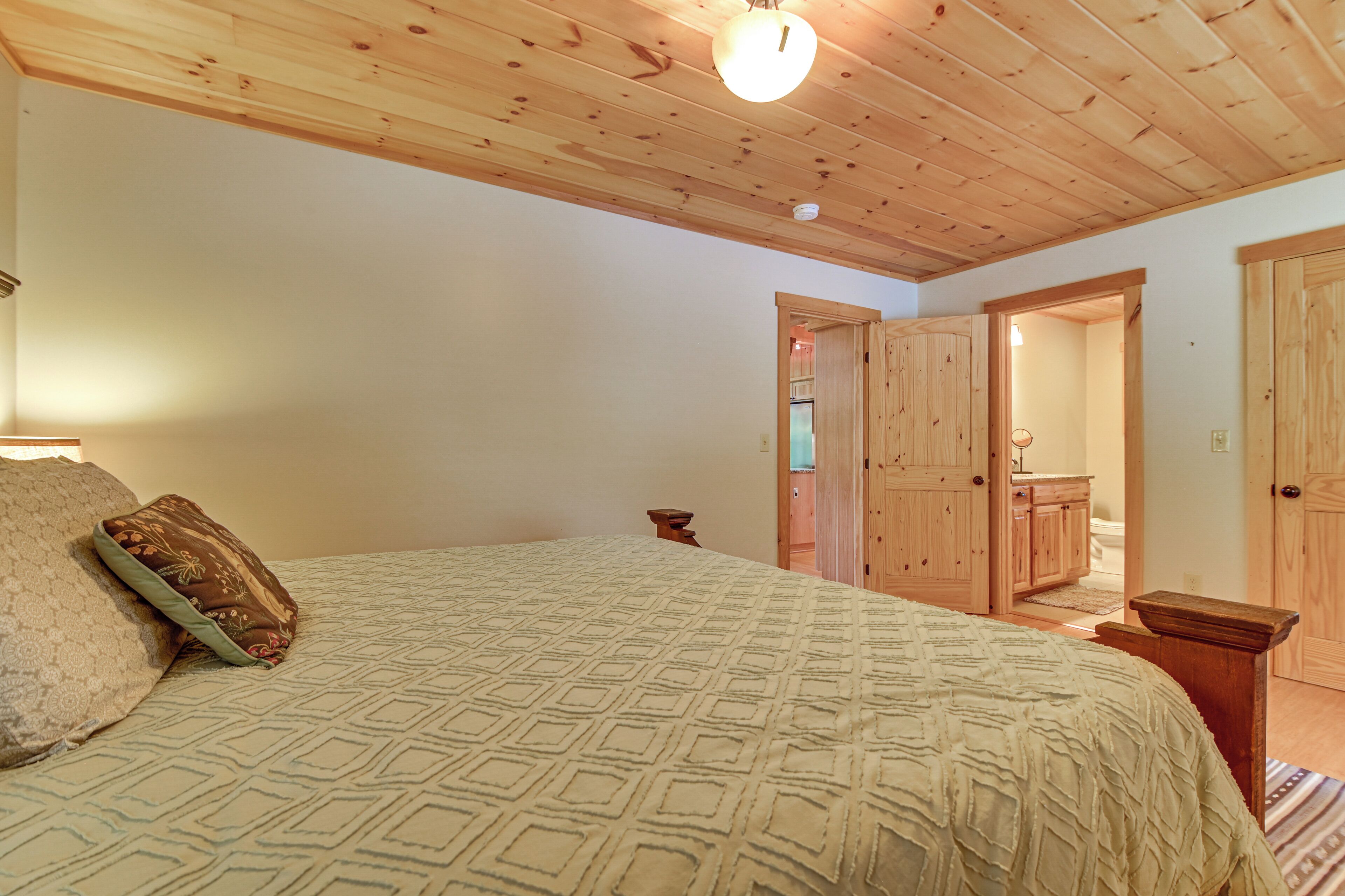 Ein Schlafzimmer mit Holzboden, einem Bett mit gemusterten Betttextilien, einem Nachttisch und einer Tür zu einem anderen Raum.