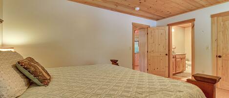 Ein Schlafzimmer mit Holzboden, einem Bett mit gemusterten Betttextilien, einem Nachttisch und einer Tür zu einem anderen Raum.