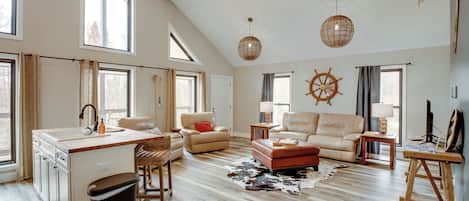 A spacious living room with a large window, a kitchen area, and a cozy seating arrangement.