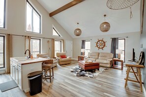 Ein geräumiges Wohnzimmer mit Küchenbereich, großen Fenstern und einer Decke mit freiliegenden Balken.