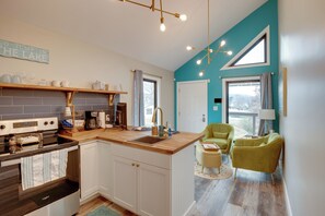 A modern kitchen with a wooden countertop, white cabinets, and a built-in oven. There is a window with curtains, a green chair, and a teal accent wall. - Boat Dock & Deck! Lake Guntersville Family Escape (Guntersville)