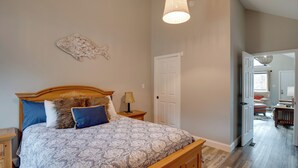 A bedroom with a wooden bed, a nightstand, a lamp, a wall art piece, and a door leading to another room. - Boat Dock & Deck! Lake Guntersville Family Escape (Guntersville)