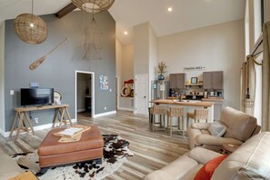 Ein modernes Wohnzimmer mit einer Ledersofa, einem Holztisch und einem Fernseher auf einem Holzboden. Es gibt eine Küchenzeile mit einem Esstisch und Barhocker.