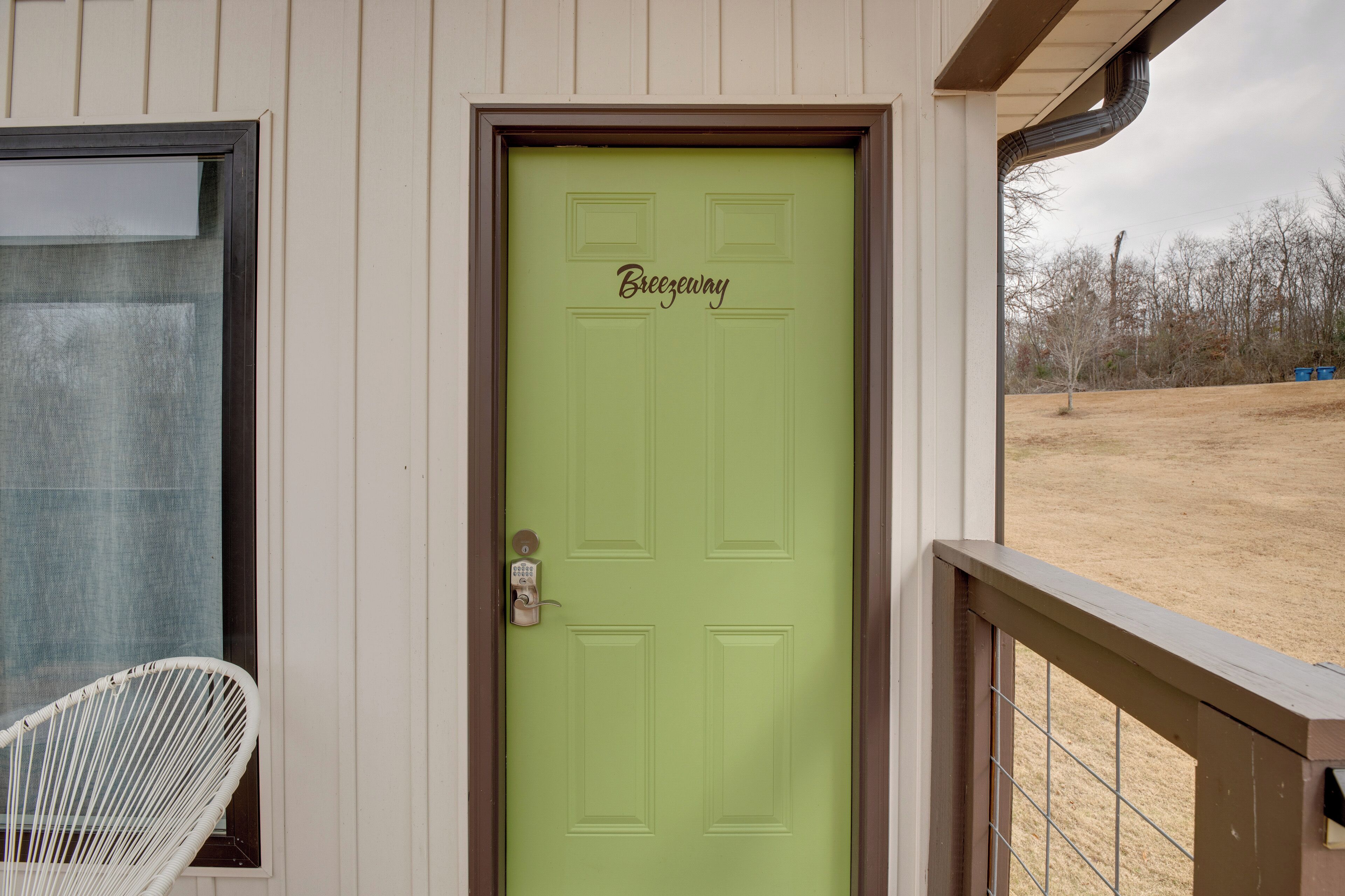 Una puerta verde con el nombre "Breezeway", una silla blanca afuera y una barandilla de madera para terraza.
