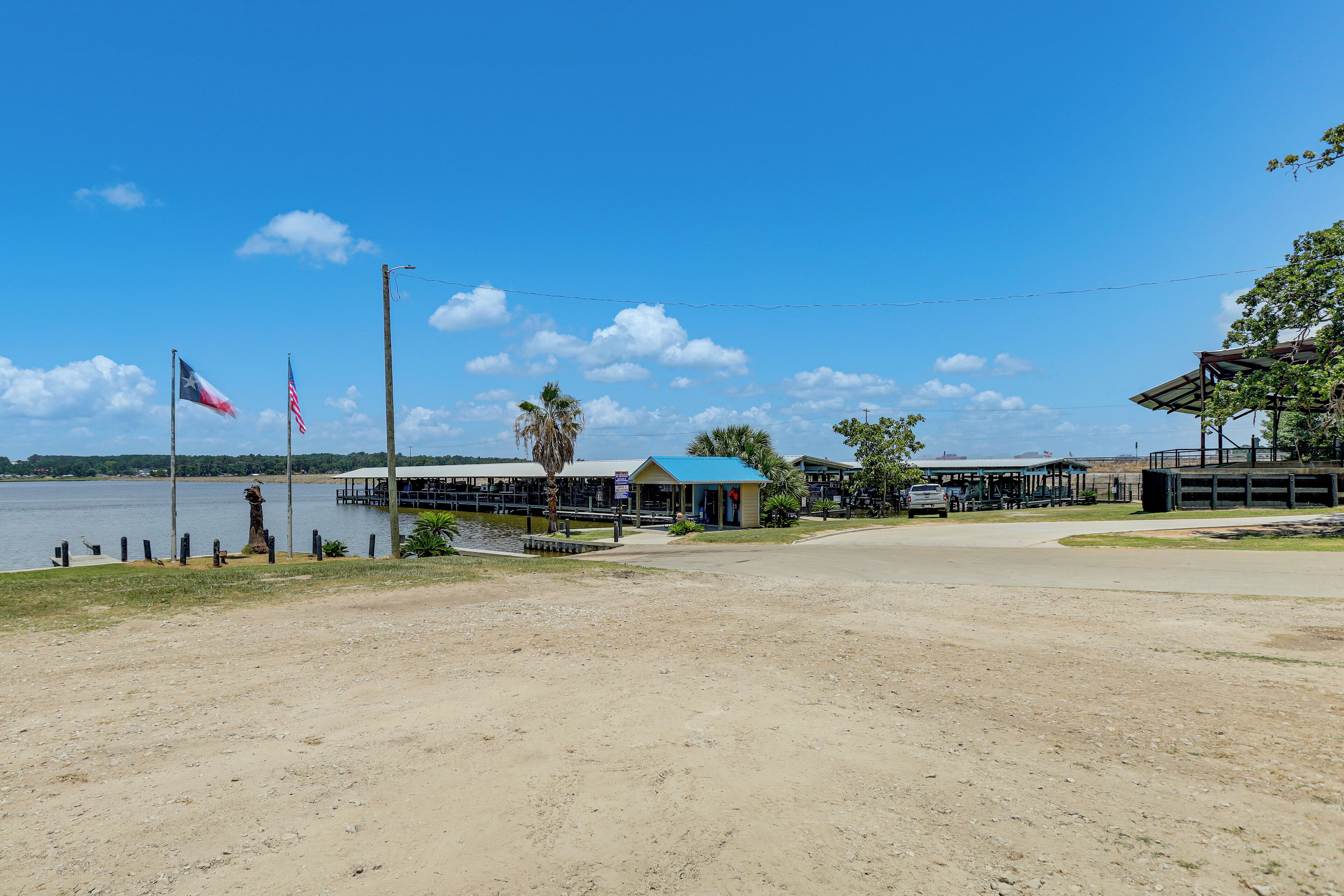 A waterfront property with a dirt path, a small building with a blue roof, and two flags.