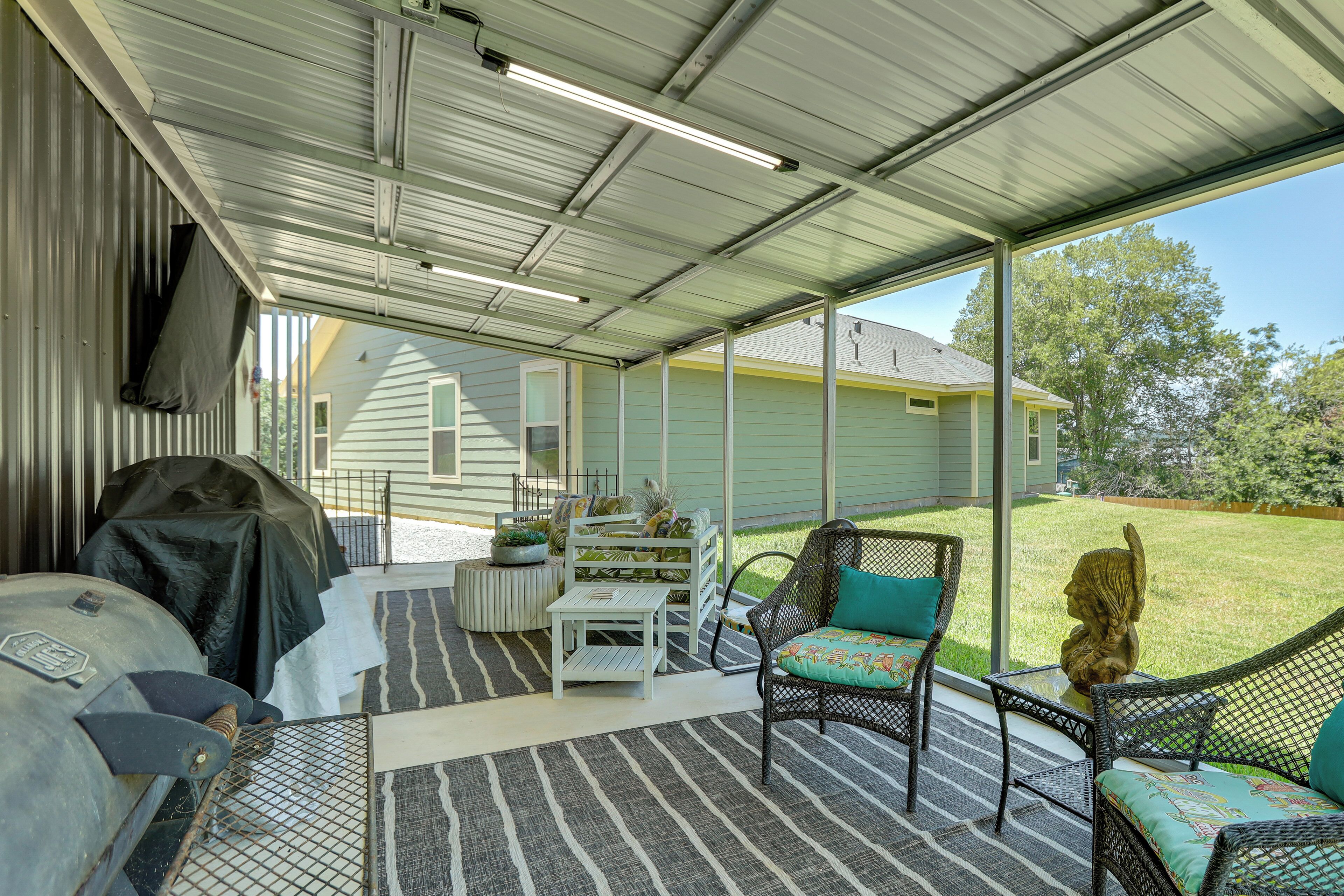 Un porche cubierto con muebles de exterior, una parrilla y vistas a una casa.