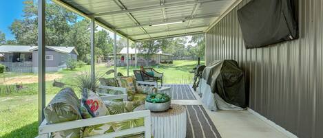 A covered patio area with a white bench, a round table with a plant, and a view of a house and yard.