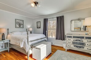 Ein Schlafzimmer mit Bett, Nachttischen, einem Schminktisch, einem Fenster mit Vorhängen und Bildern an den Wänden.