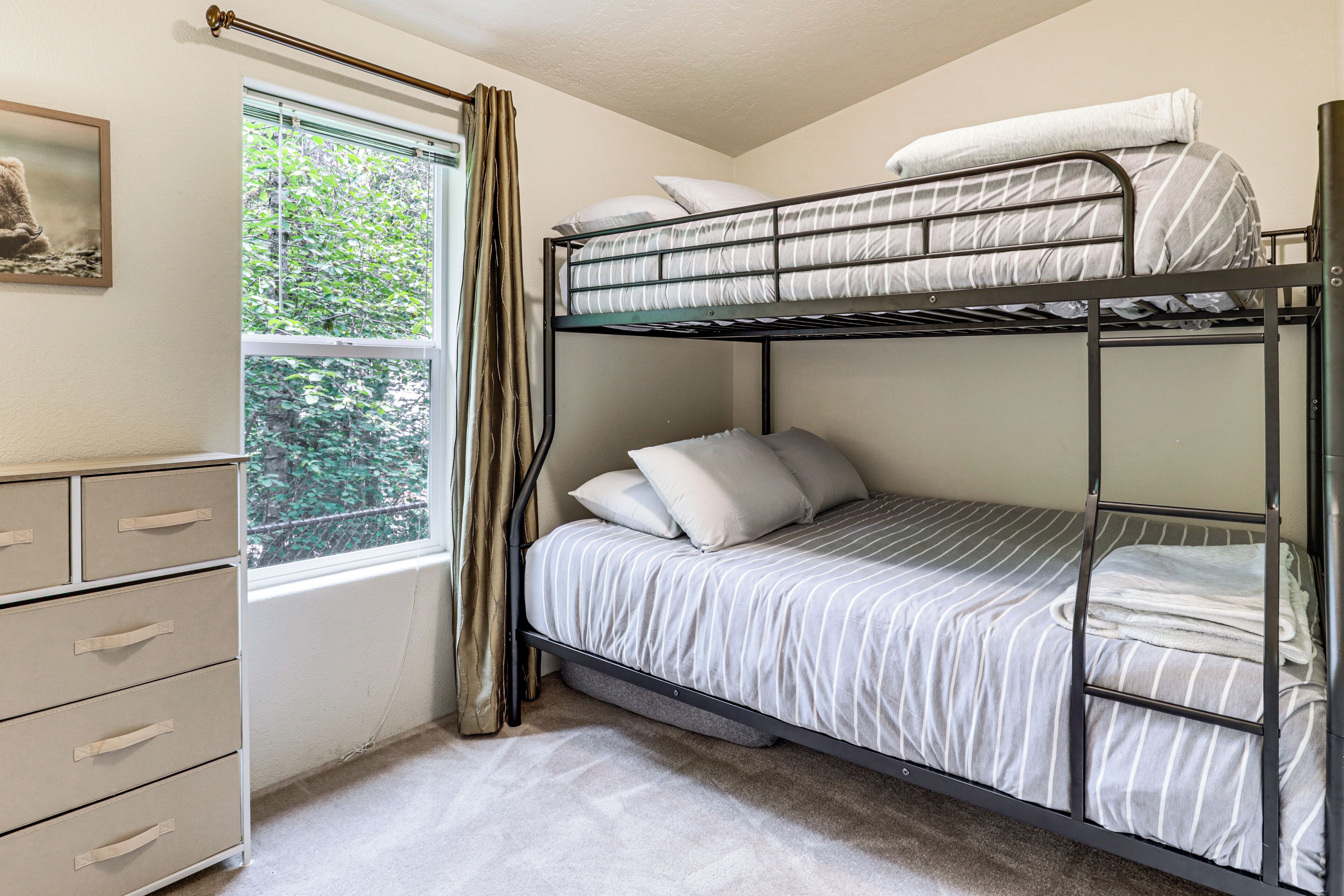Une chambre avec un lit superposé, une fenêtre, une commode et un rideau.