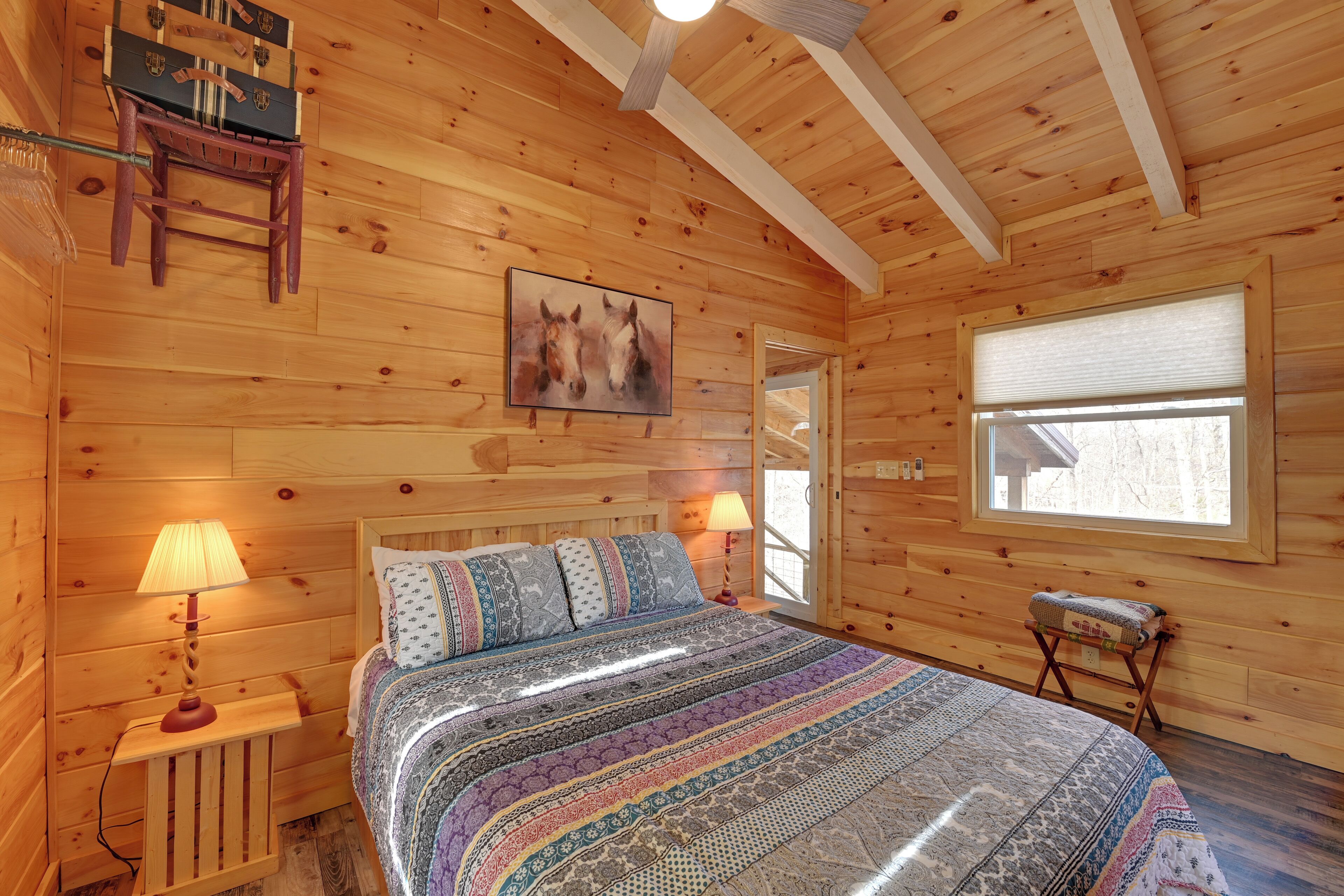 Ein Schlafzimmer einer Holzhütte mit einem Bett, zwei Nachttischlampen, einem gerahmten Gemälde, einem Fenster und einem kleinen Tisch mit einer Lampe.