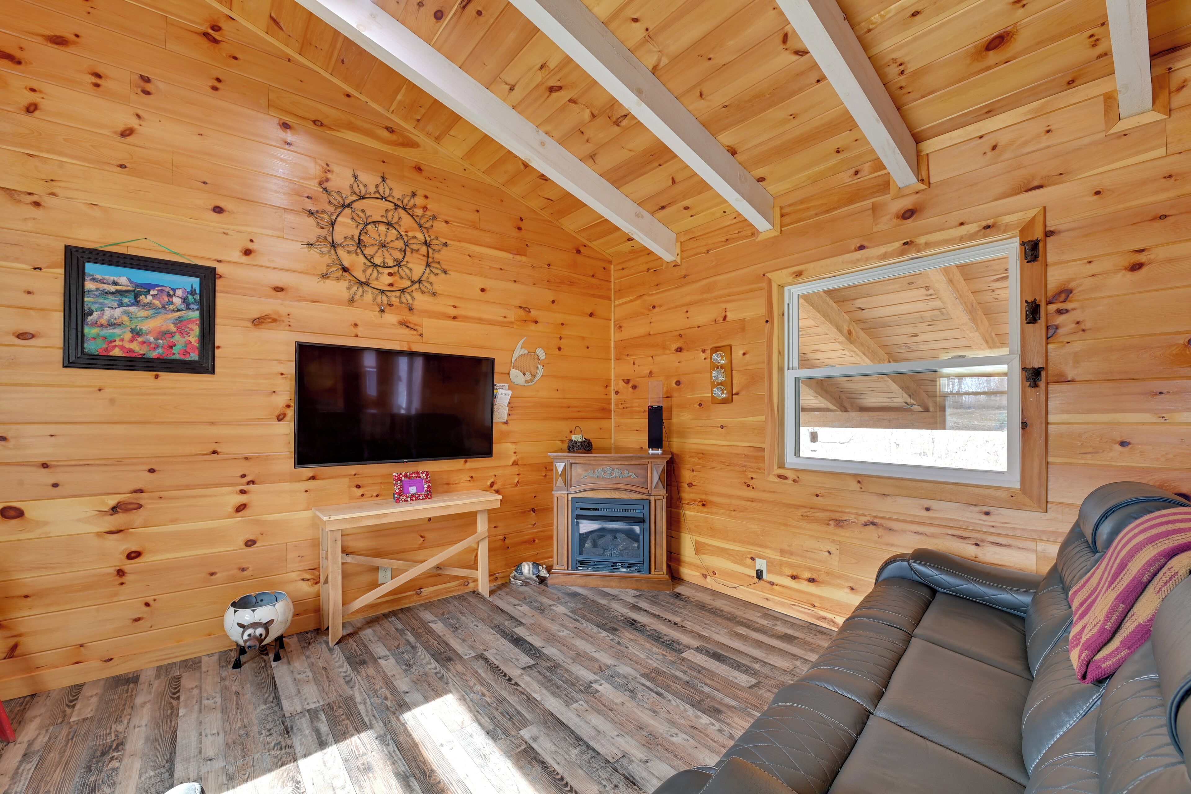 A wooden cabin interior with a TV, fireplace, sofa, and wooden walls.