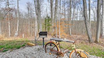A rustic wooden bench with a metal frame, a vintage bicycle, and a metal bird feeder in a forested area.