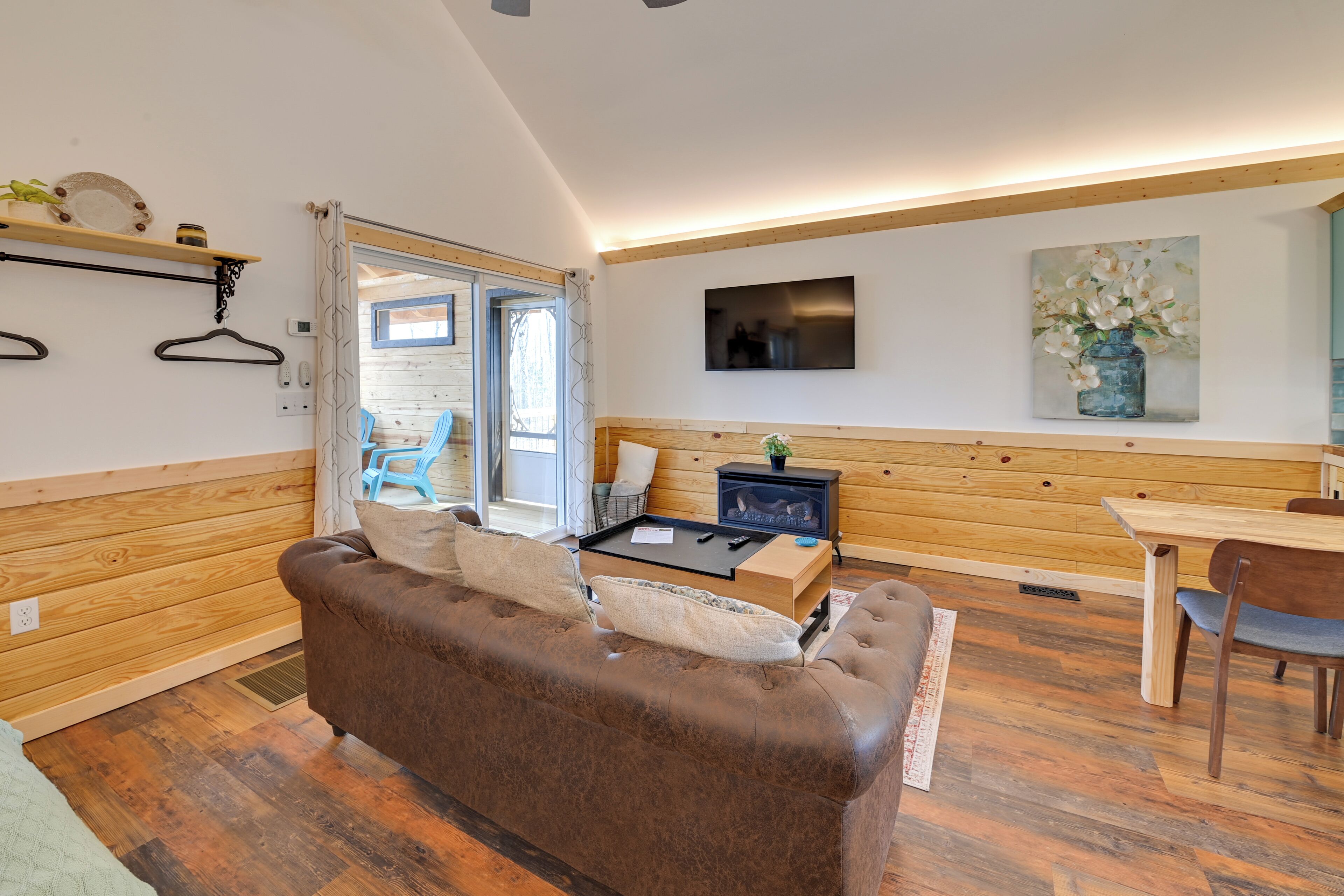 A cozy room with a brown leather sofa, a wooden dining table, and a TV mounted on the wall.