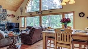 A cozy living room with a fireplace, large windows, and a dining area with wooden furniture.