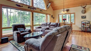 A spacious living room with a large window, a fireplace, and a ceiling with wooden beams.