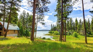 A lodge with a green roof, surrounded by tall pine trees and a lake view.