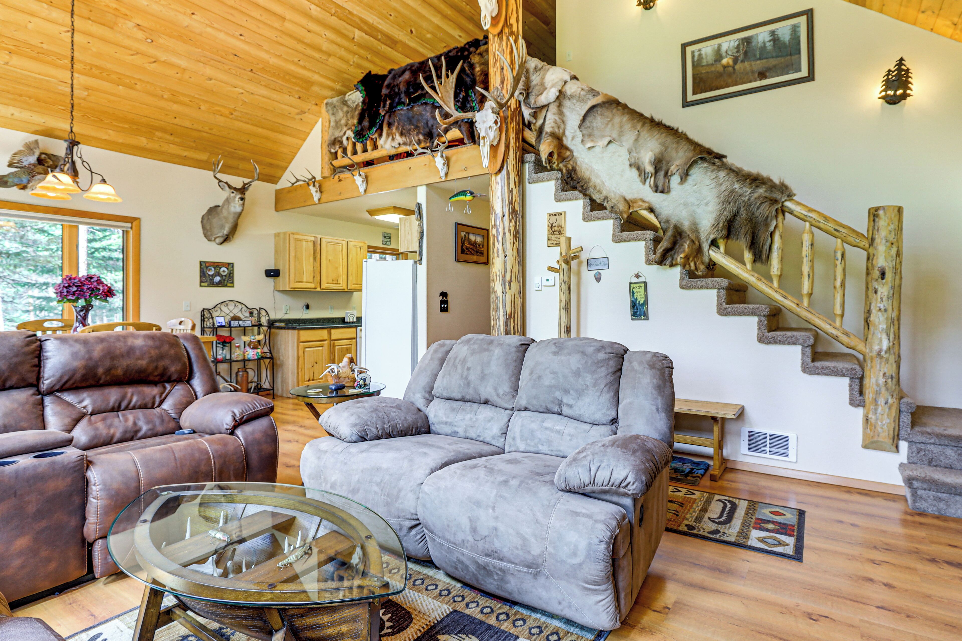 A living room with a fireplace, leather sofas, a glass coffee table, and a staircase with a mounted animal head.