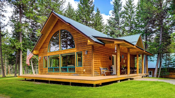A log cabin with a porch, large windows, and an American flag.