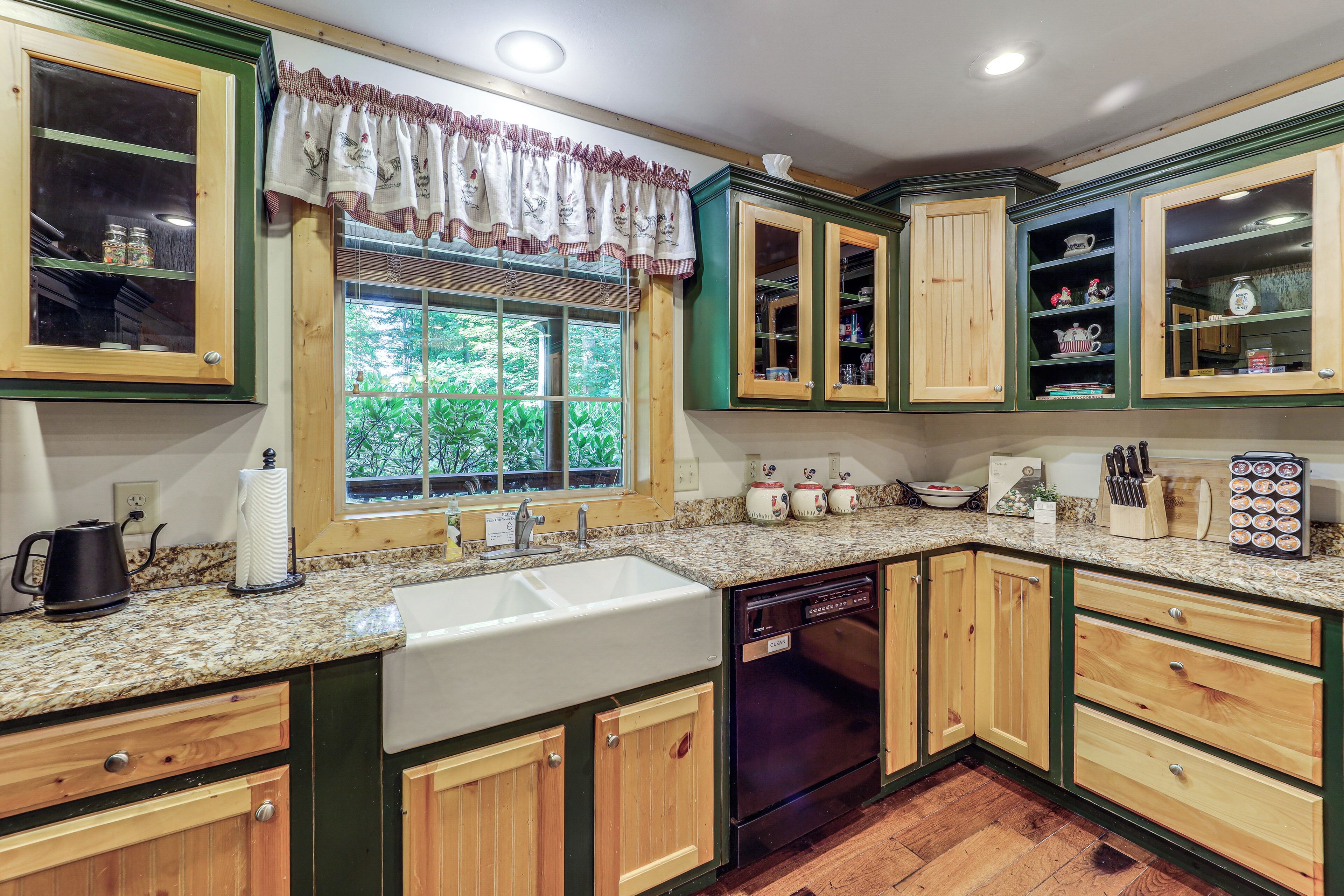 A kitchen with wooden cabinets, a sink, a dishwasher, and a window with a view of greenery.