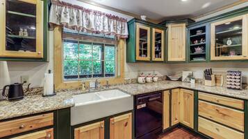 A kitchen with wooden cabinets, a sink, a dishwasher, and a window with a view of greenery.