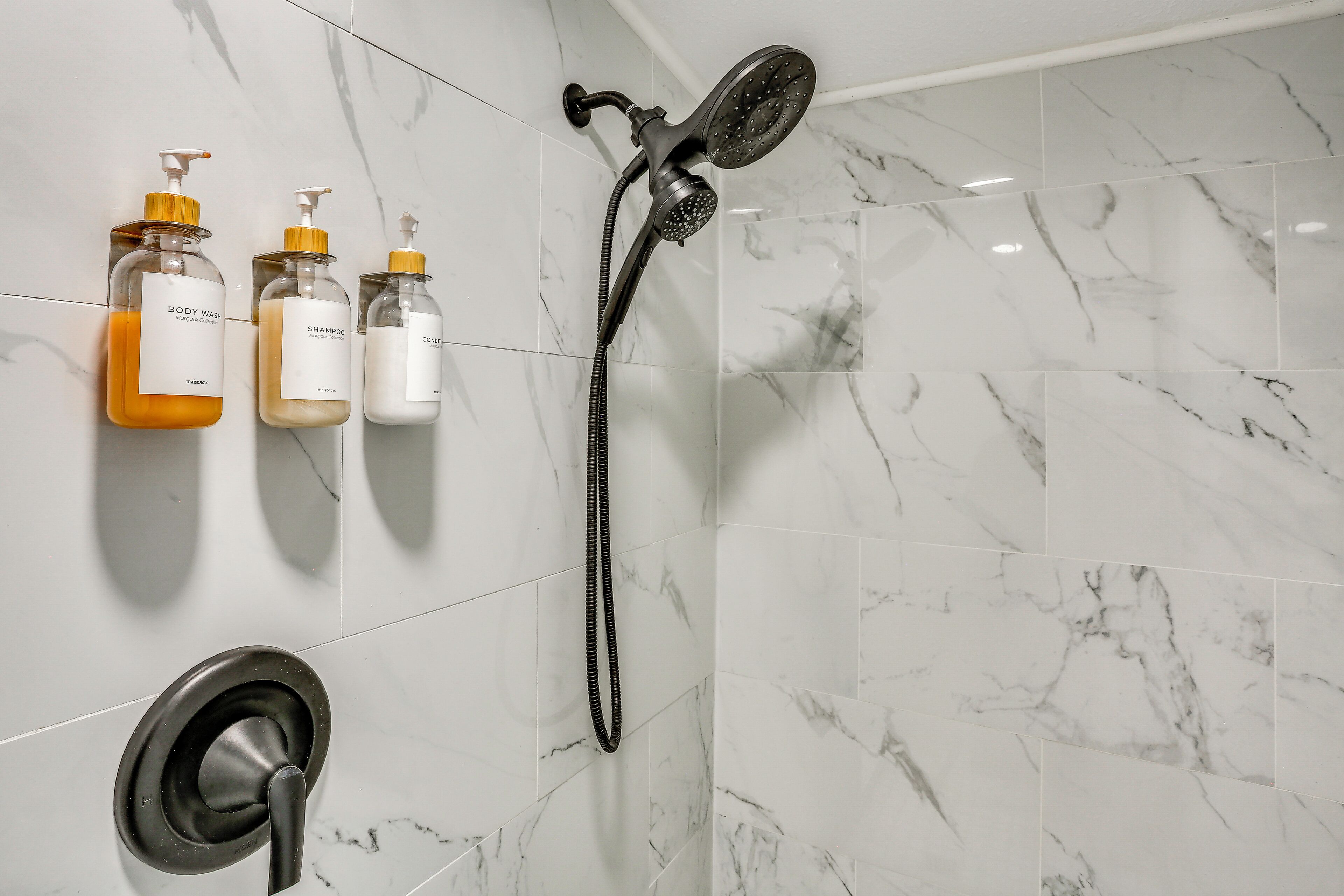 Ein Badezimmer mit Dusche, Toilette und drei Flaschen Pflegeprodukte an der Wand.