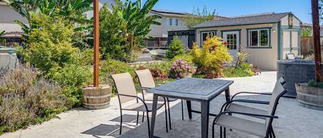 Eine Terrasse mit Tisch und Stühlen, umgeben von üppiger Bepflanzung und einem Haus im Hintergrund.