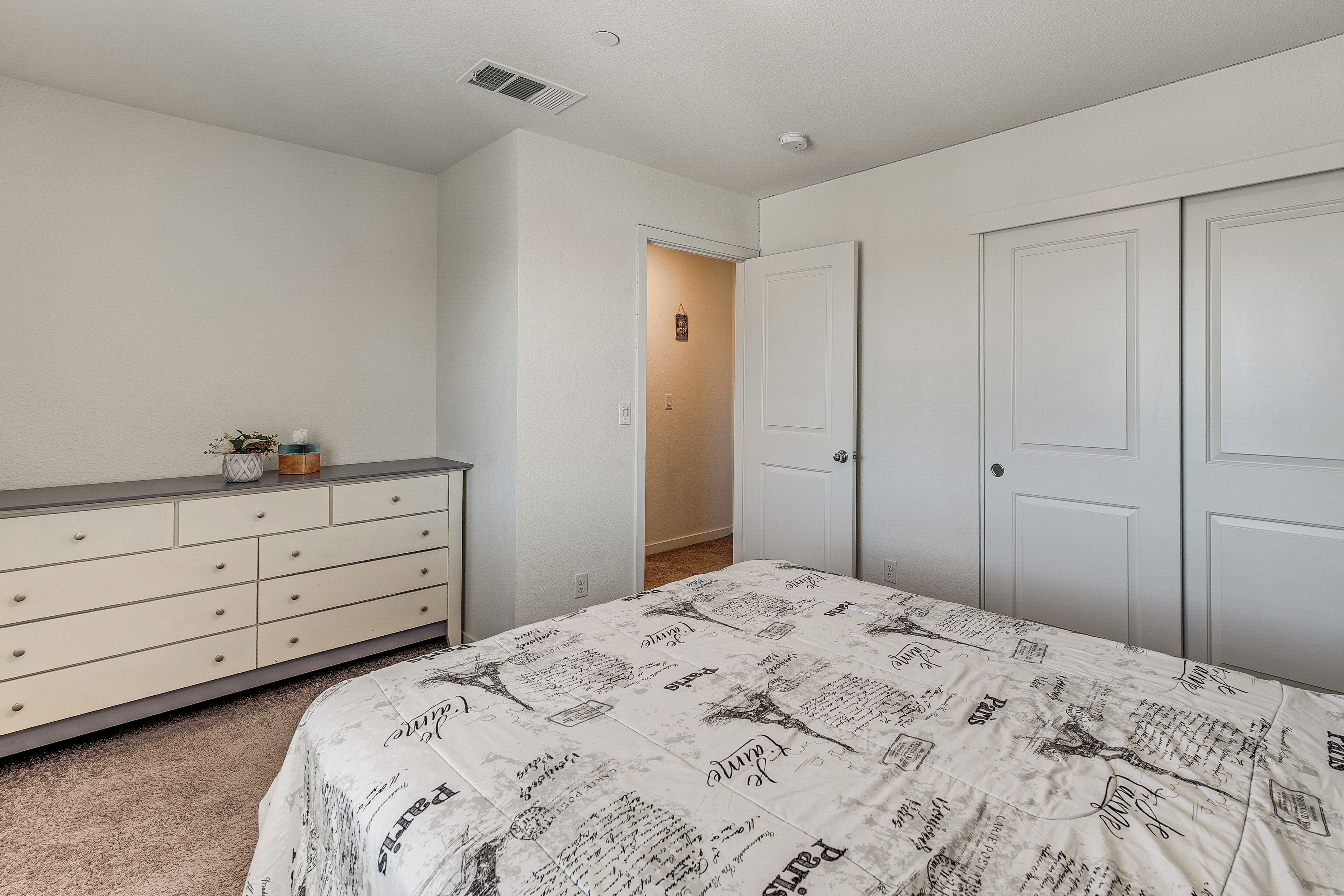 A bedroom with a bed, dresser, and two doors.