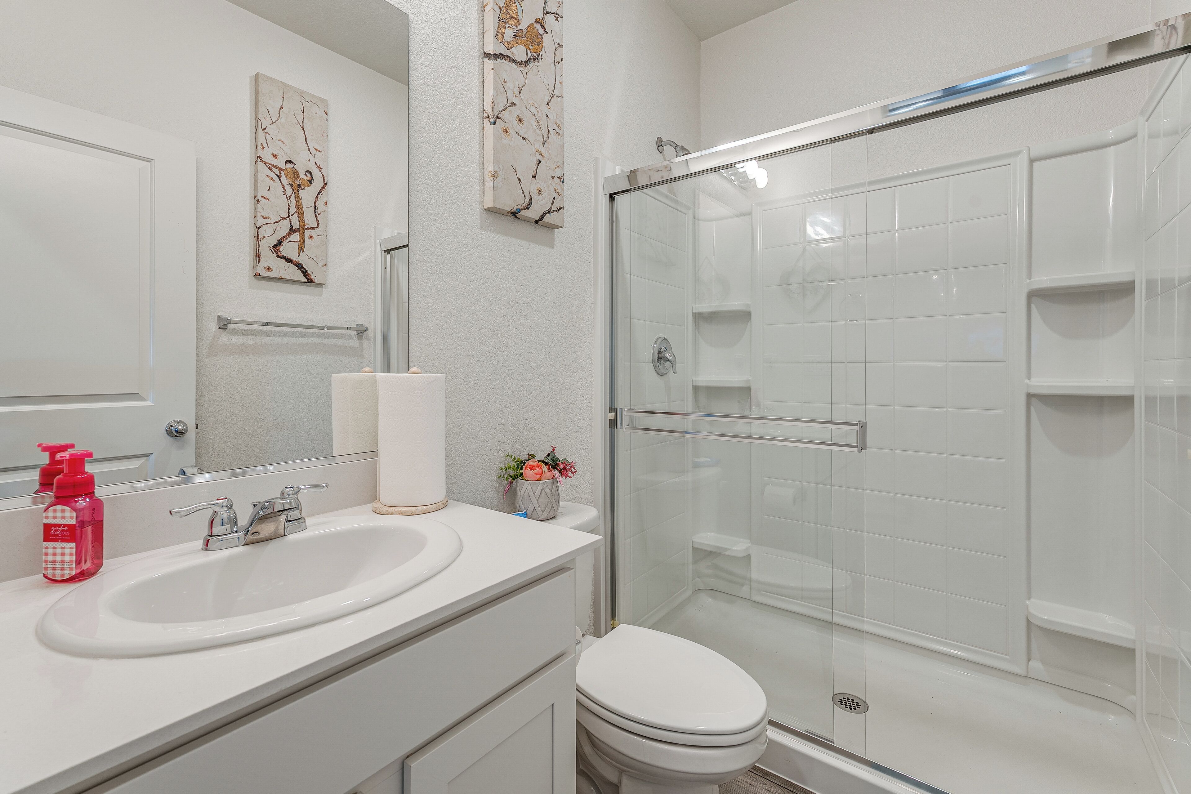 Une salle de bain avec un lavabo blanc, un miroir, des toilettes et une douche à parois de verre.