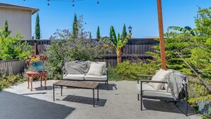 A patio with a wooden table and two cushioned chairs, a potted plant, and a string of lights. - Private Patio & Yard! Family Getaway in Stockton (Stockton)