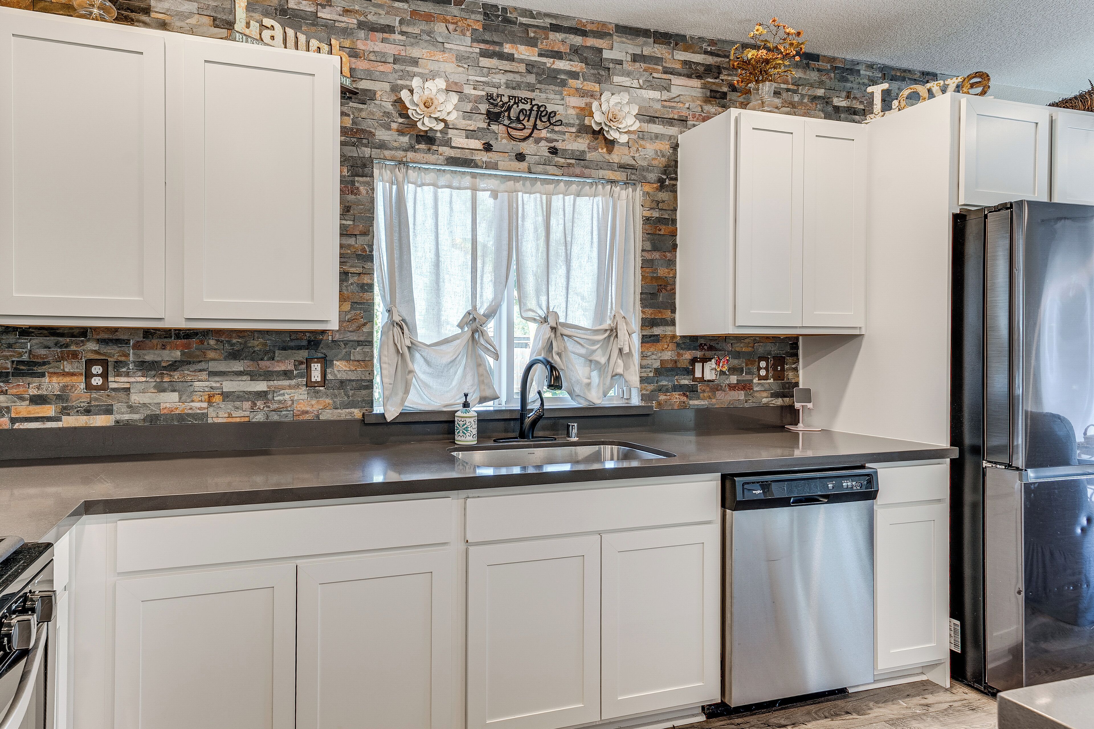A kitchen with white cabinets, a stainless steel refrigerator, a dishwasher, and a stone backsplash.