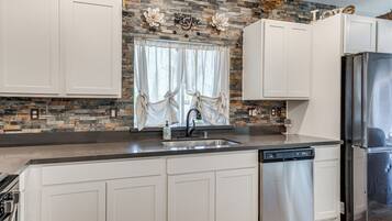 A kitchen with white cabinets, a stainless steel refrigerator, a dishwasher, and a stone backsplash.