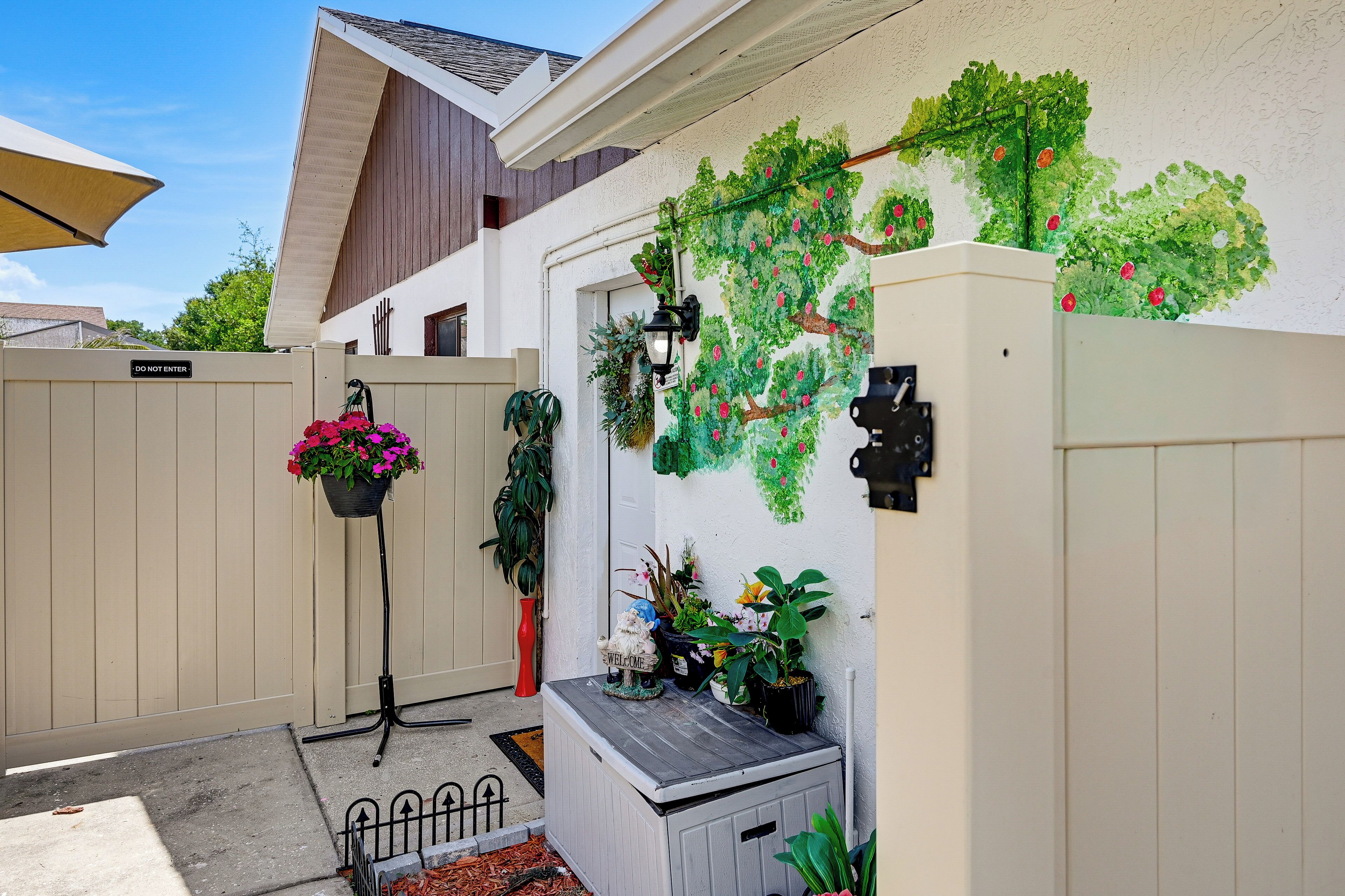 Un espace délimité par une barrière et sur lequel est apposée une pancarte indiquant « DÉFENSE D’ENTRER », un pot de fleurs orné de fleurs roses et un jardinier mural agrémenté de feuillage vert.