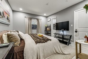 Ein Schlafzimmer mit einem Bett, einem Schreibtisch, einem Fernseher und einem Fenster mit Vorhängen.
