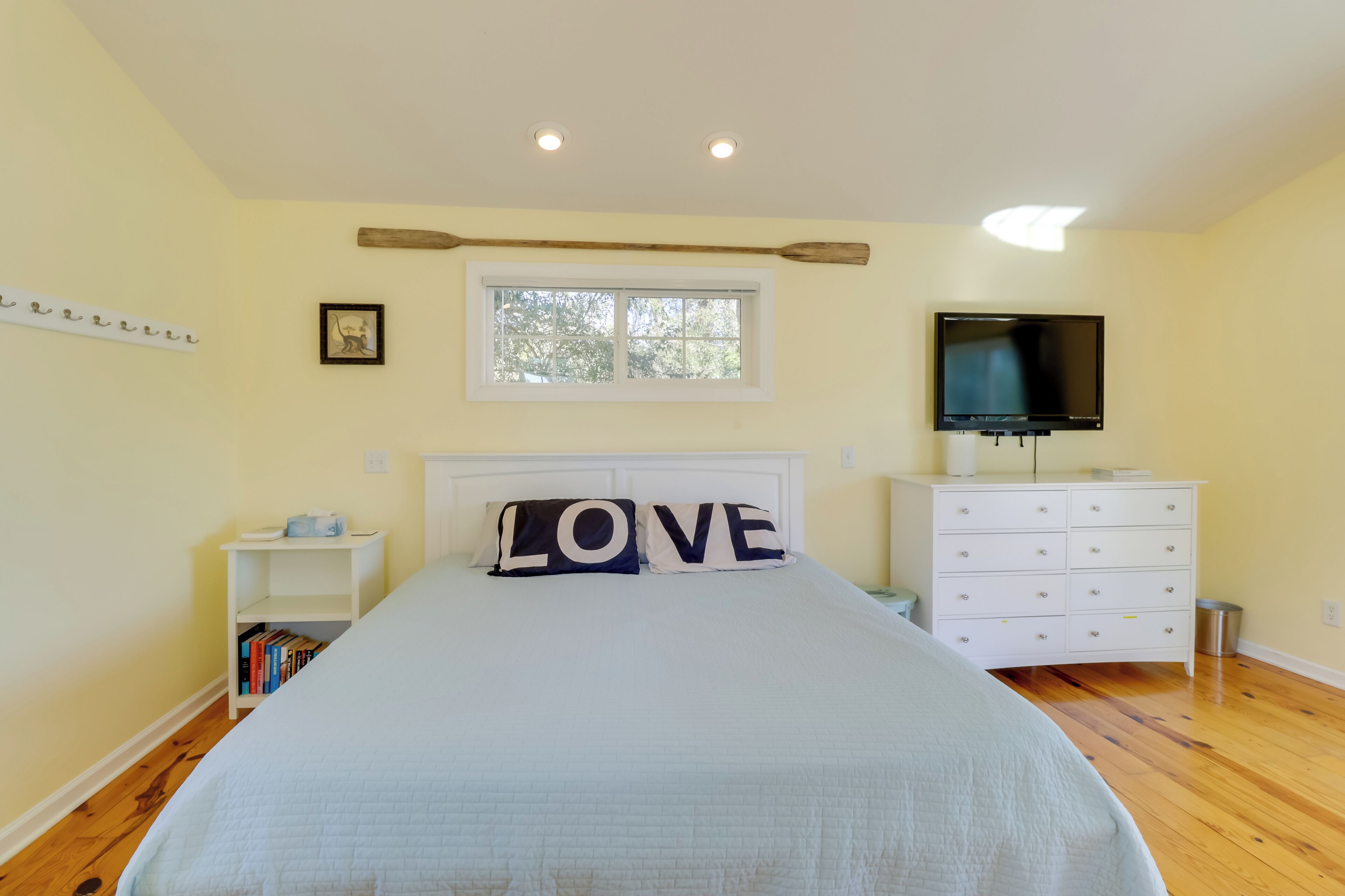 A bedroom with a bed, a TV, a dresser, a nightstand, and a window.