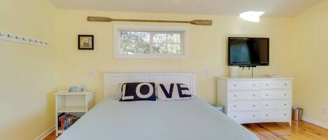 A bedroom with a bed, a TV, a dresser, a nightstand, and a window.