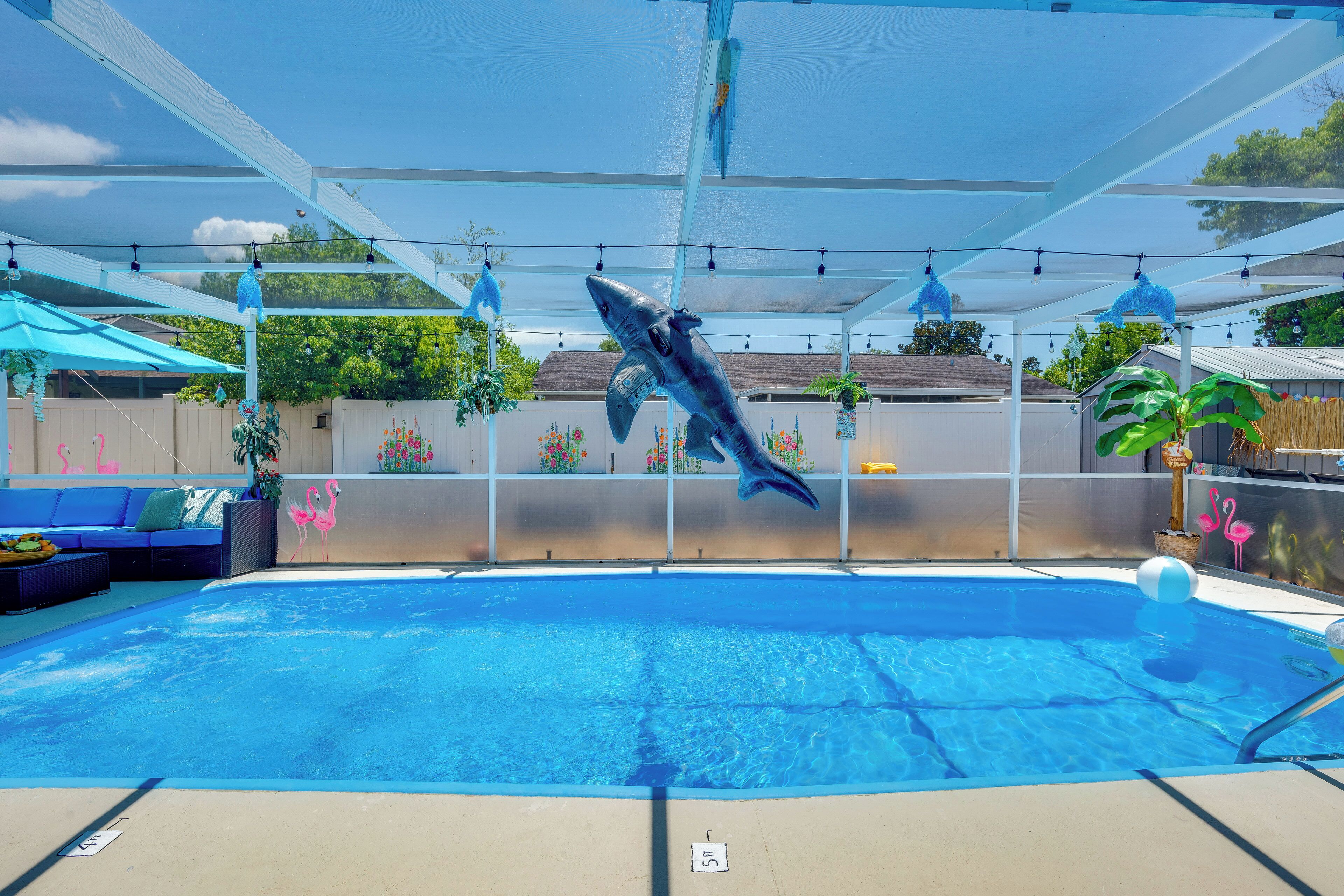 A swimming pool with a dolphin sculpture, a covered patio, and a blue umbrella.
