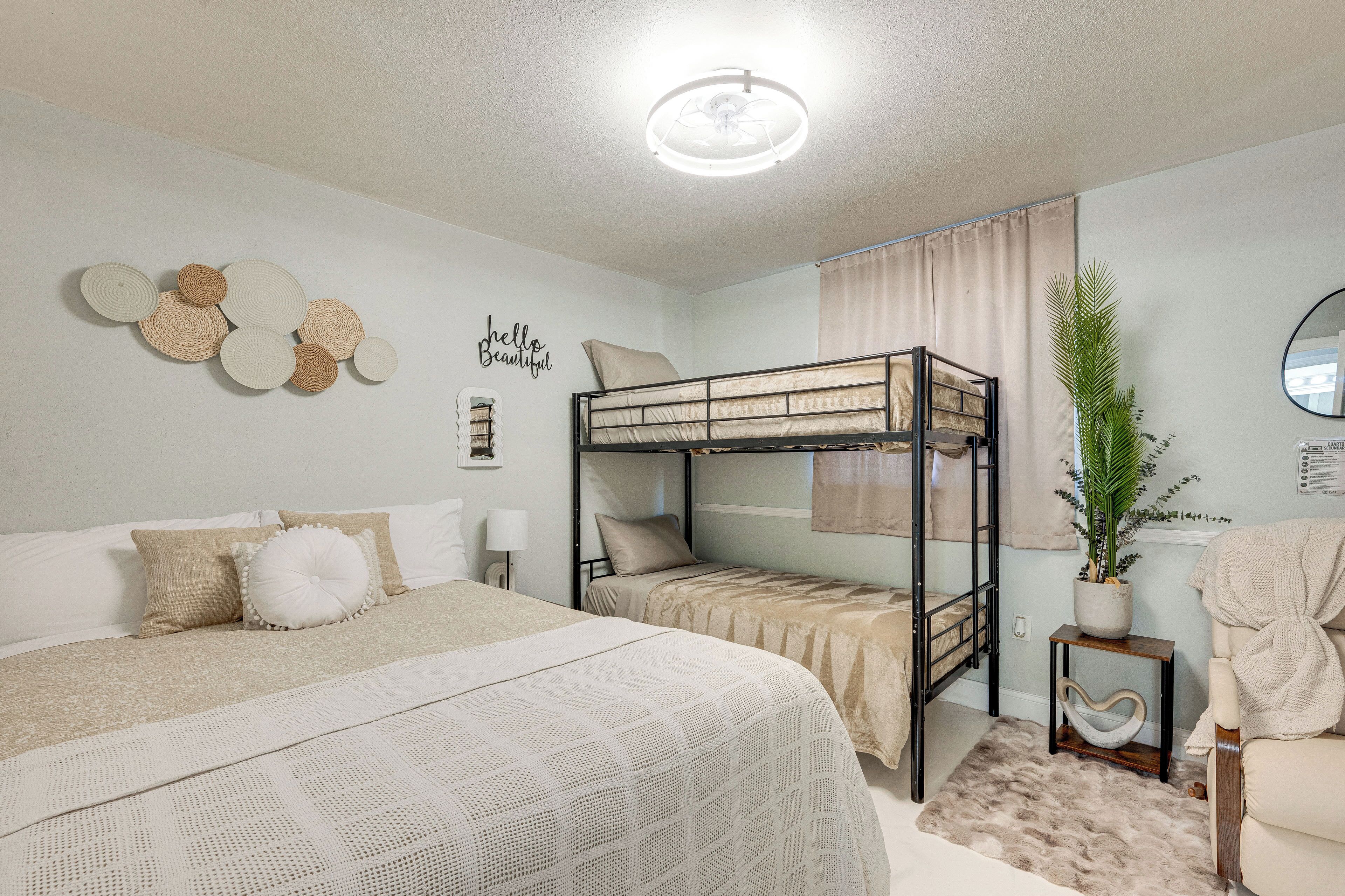 A bunk bed room with a white bed, a bedside table, a mirror, and a potted plant.