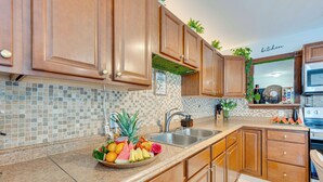 A kitchen with wooden cabinets, a tiled backsplash, a fruit bowl, a sink, and a microwave. - Fun in the Sun! Vibrant Port Richey Home w/ Lanai (Port Richey)