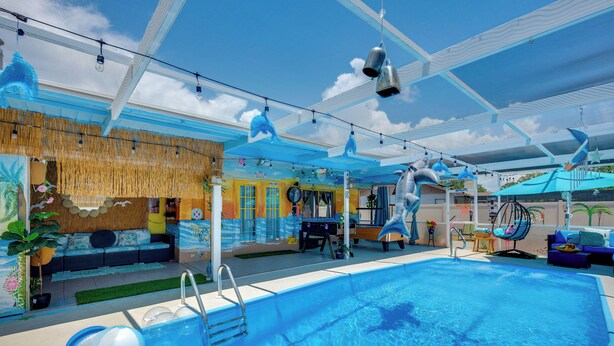An indoor swimming pool with clear blue water, a sunroof, and a seating area with a tropical theme. - Fun in the Sun! Vibrant Port Richey Home w/ Lanai (Port Richey)