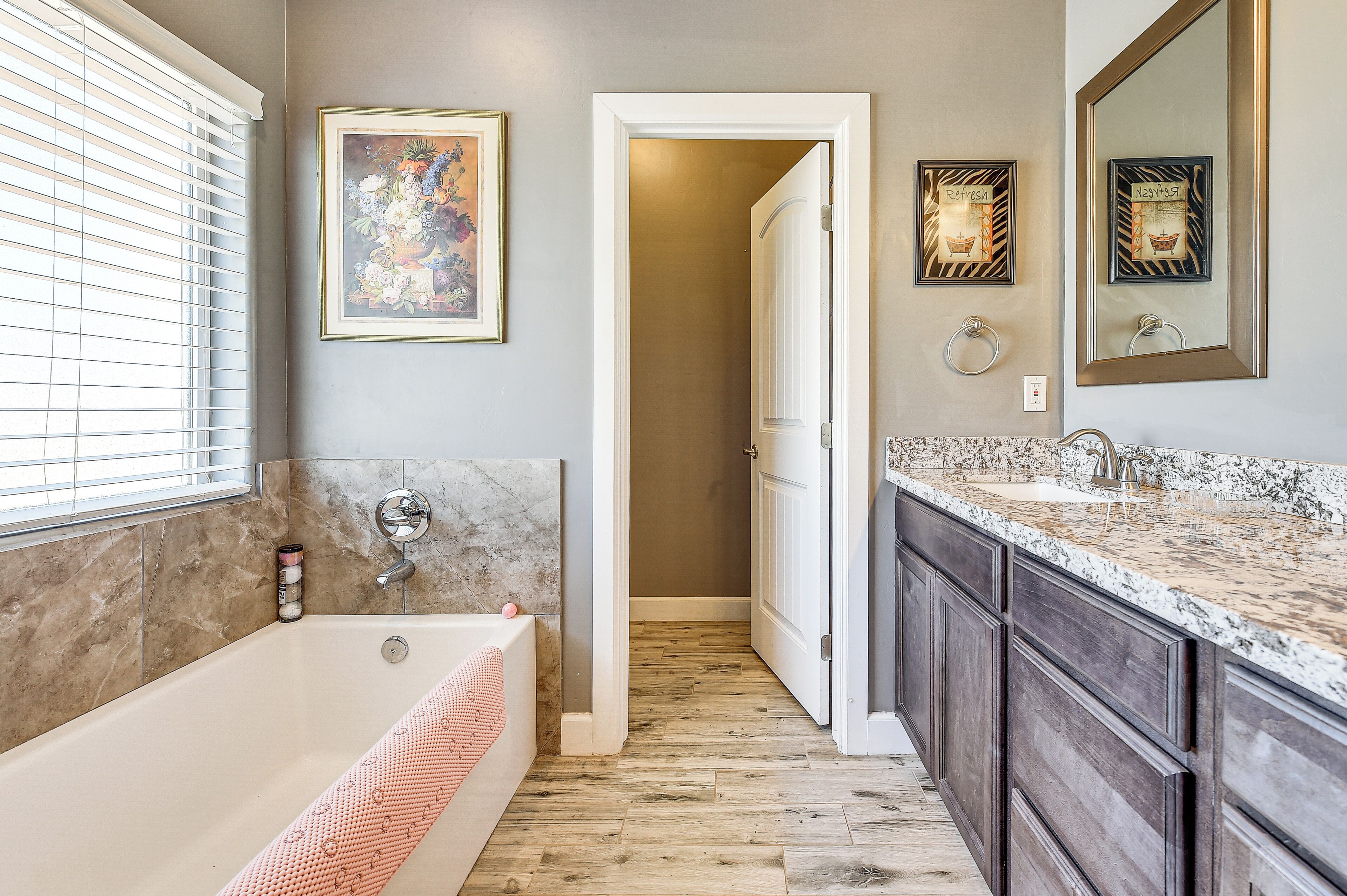 A bathroom with a bathtub, a vanity with a sink, a mirror, and a framed artwork on the wall.