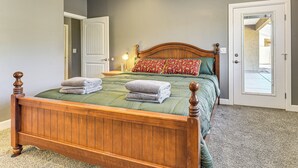 Quarto com cama de madeira, roupa de cama verde e almofada estampada vermelha.