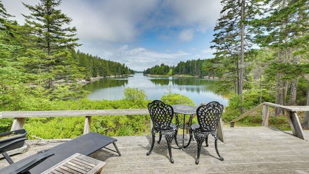 Eine Holzterrasse mit Tisch und Stühlen mit Blick auf einen von Bäumen gesäumten See.