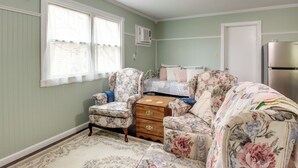 Une chambre à coucher avec un lit à motifs floraux, un fauteuil assorti, une commode et une fenêtre avec des stores.