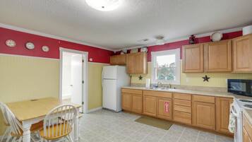 A compact kitchen with wooden cabinets, a refrigerator, a microwave, and a dining area with a table and chairs.