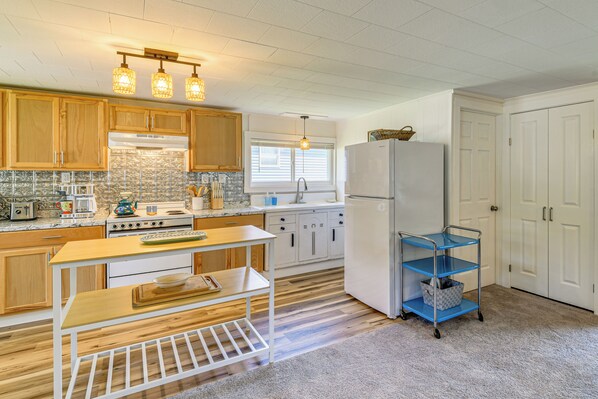 A modern kitchen with wooden cabinets, a white refrigerator, a blue cart, and a window with blinds. - Fire Pit, Private Dock! Lamoka Lake Retreat (Bradford)
