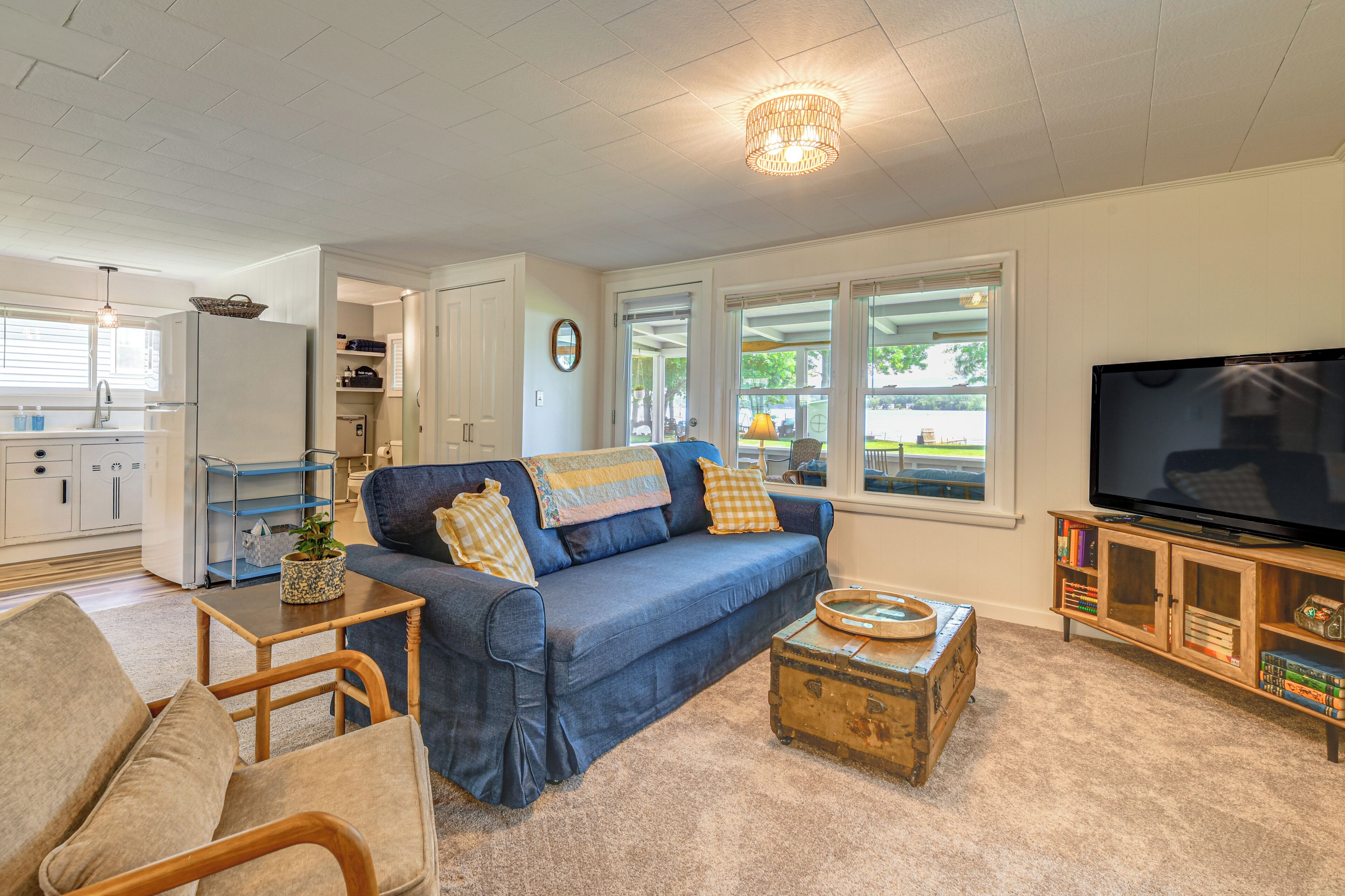 A living room with a sofa, coffee table, and television. There is a kitchen in the background.