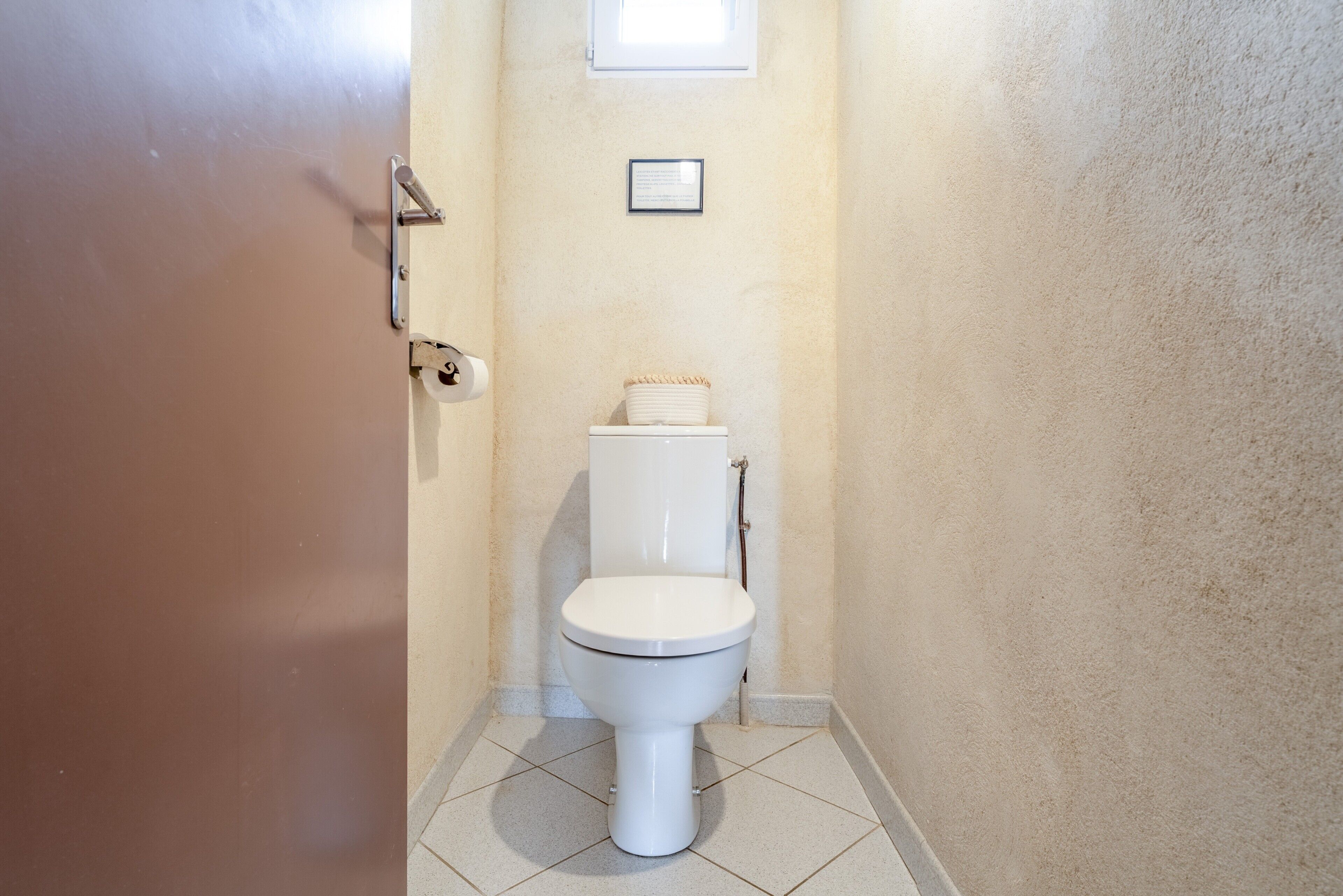 A bathroom with a toilet, a roll of toilet paper, and a framed item on the wall.