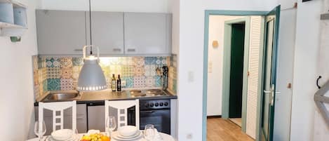 Une cuisine compacte avec un mur recouvert de carreaux, une table à manger pour quatre personnes et une vue sur une pièce dont la porte est peinte en vert.