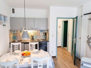 A compact kitchen with a tiled backsplash, a dining table set for four, and a view into a room with a green door. - FeWo Tannenrauschen im Ferienpark Hahnenklee (Goslar)